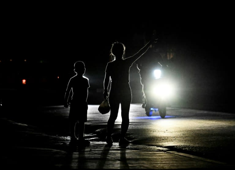Una mujer hace una señal a un automovilista en la oscuridad durante un apagón en Bauta, provincia de Artemisa, Cuba, el 18 de marzo de 2024. (YAMIL LAGE)
