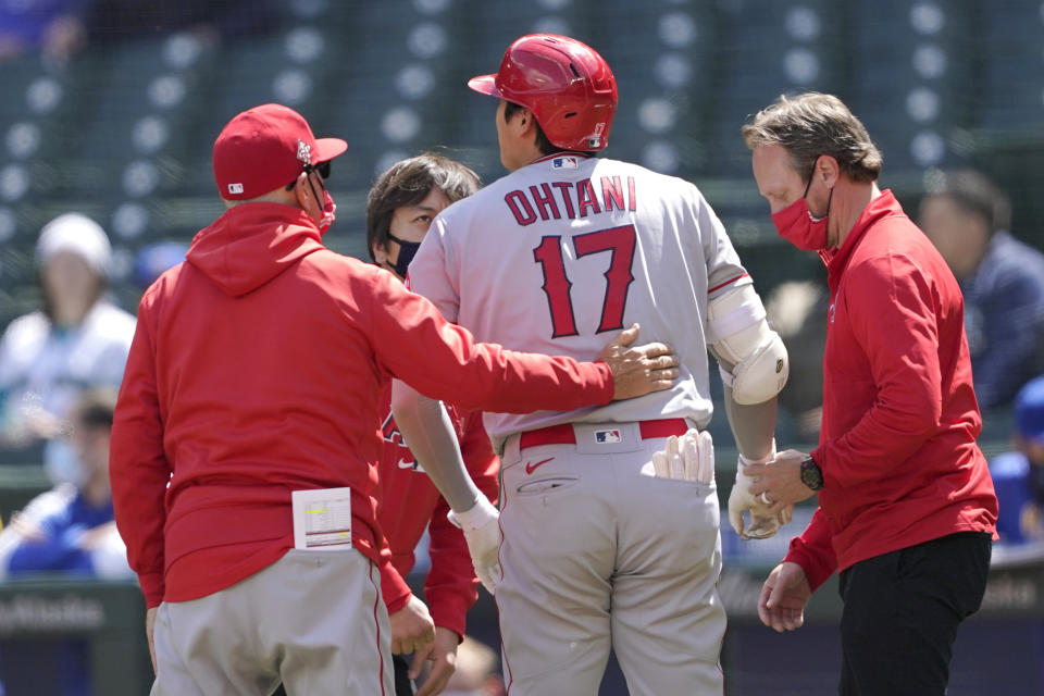 Los Angeles Angels Shohei Ohtani (17), talks with a trainer, right, and manager Joe Maddon, left, after he was hit by a pitch during the first inning of a baseball game against the Seattle Mariners, Sunday, May 2, 2021, in Seattle. Ohtani stayed in the game. (AP Photo/Ted S. Warren)