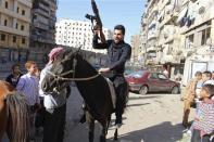 A Free Syrian Army fighter holds up his weapon and rides a horse as people on the first day of Eid al-Adha in Aleppo October 15, 2013. REUTERS/Molhem Barakat