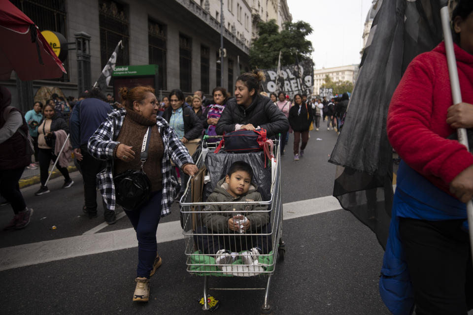 A woman pushes her son in a shopping cart during a protest to demand jobs, social benefits for the unemployed, and more food for soup kitchens amidst skyrocketing inflation, in Buenos Aires, Argentina, Thursday, Aug. 24, 2023. (AP Photo/Victor R. Caivano)