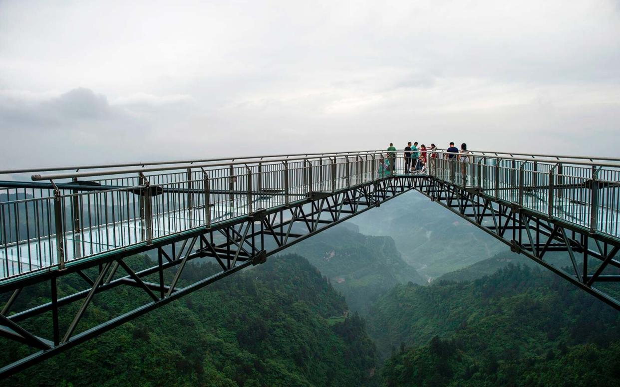 Tourists look on from a glass-bottomed skywalk.