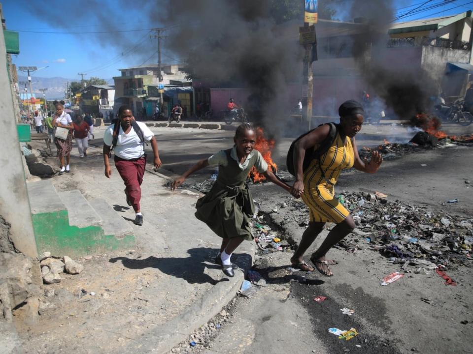 A woman and her daughter run past a barricade set up by police during a protest to denounce bad police governance in Port-au-Prince, Haiti on Jan. 26, 2023. (Odelyn Joseph/The Associated Press - image credit)