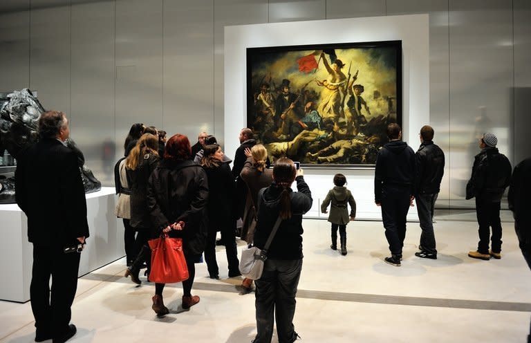 People stand in front of Eugene Delacroix's masterpiece "Liberty Leading the People" on display in Lens, northern France, on December 4, 2012. Specialists have been able to "completely remove" marks left by a defacement of one of the most iconic paintings in French history, according to the Louvre