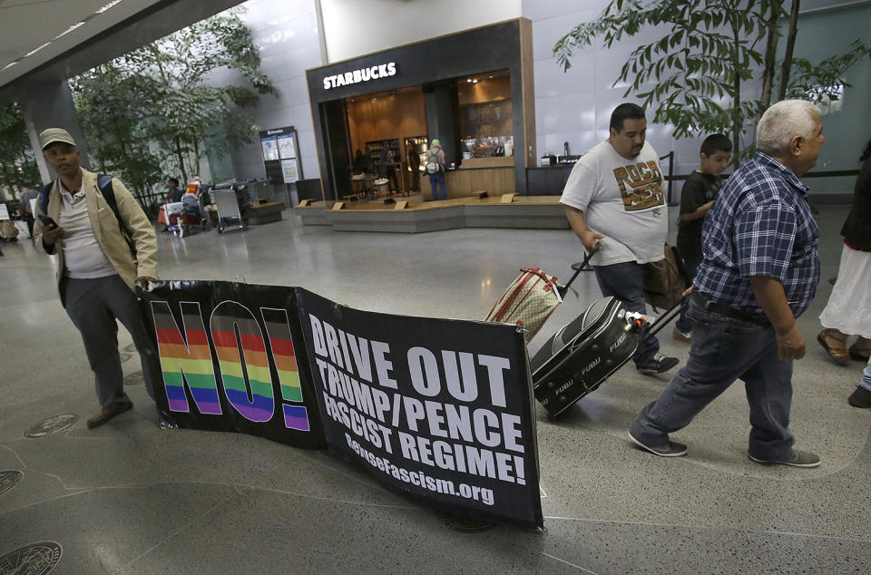 <p>Protester Xochitl Johnson, left, holds up a sign as travelers walk past at San Francisco International Airport in San Francisco, June 29, 2017. A scaled-back version of President Donald Trump’s travel ban takes effect Thursday evening, stripped of provisions that brought protests and chaos at airports worldwide in January yet still likely to generate a new round of court fights. (AP Photo/Jeff Chiu) </p>