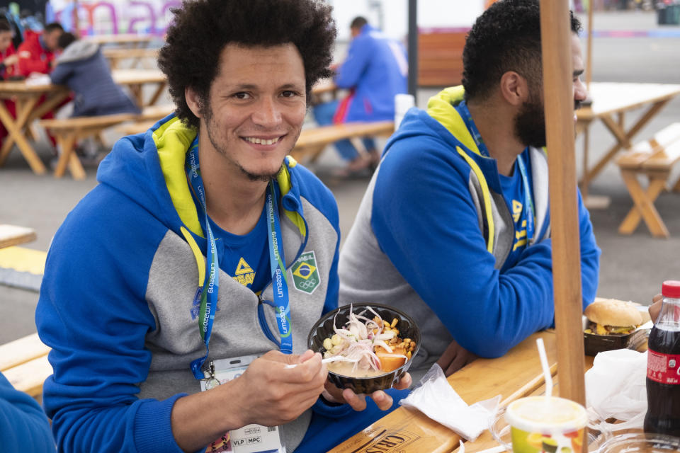 In this Aug. 3, 2019 photo, Thiagus Petrus, a member of the Brazilian handball team poses for photos while he takes a break from eating ceviche at the international center outside the Pan American athletes' village in Lima, Peru. Peruvian food was the star at the recent Pan Am Games. Athletes from 41 countries across the Americas tasted the highly-regarded cuisine that blends indigenous traditions with European, African and Asian influences with an abundance of seafood from the Pacific Ocean’s cold Humboldt current. (AP Photo/Luis Andres Henao)