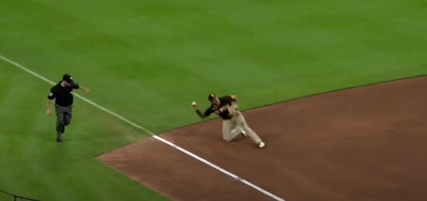 Manny Machado throws a baseball while on one knee