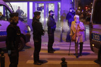 A woman crosses a street as police surround a bar they raid in Warsaw, Poland, Friday March 26, 2021. A raft of new pandemic restrictions take effect in Poland on Saturday to slow the spread of infection in what has become of the new global hot spot for the virus, but even earlier restrictions are being defied by some.(AP Photo/Czarek Sokolowski)