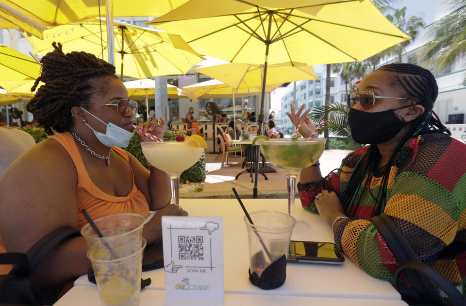 Anita Anderson, left, of Grand Rapids, Mich., and her niece Tawnya Heggins of Houston, chat as they dine outside a restaurant on Miami Beach, Florida's famed South Beach, Friday, June 26, 2020. Florida banned alcohol consumption at its bars Friday as its daily confirmed coronavirus cases neared 9,000, a new record that is almost double the previous mark set just two days ago. (AP Photo/Wilfredo Lee)
