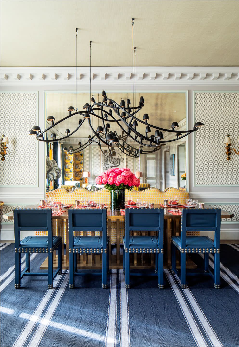 blue dining chairs surround a dining table with orange place settings and pink peonies