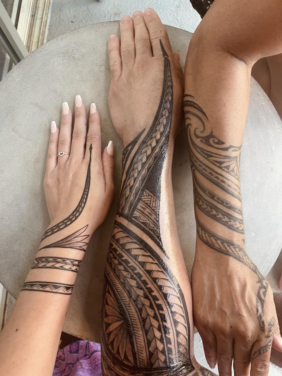 Three arms with intricate tribal-style tattoos, one arm with fresh ink, the other healed