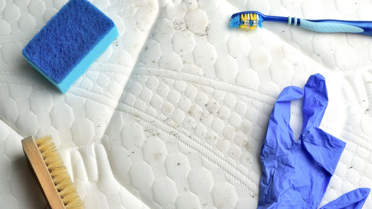  Image shows black mold on a white mattress being cleaned with alcohol, brushes and sponges. 