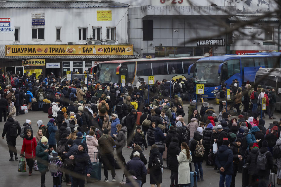 Large numbers of Ukrainian in warm clothes and hats gather around buses in front of a shawarma restaurant and bar.