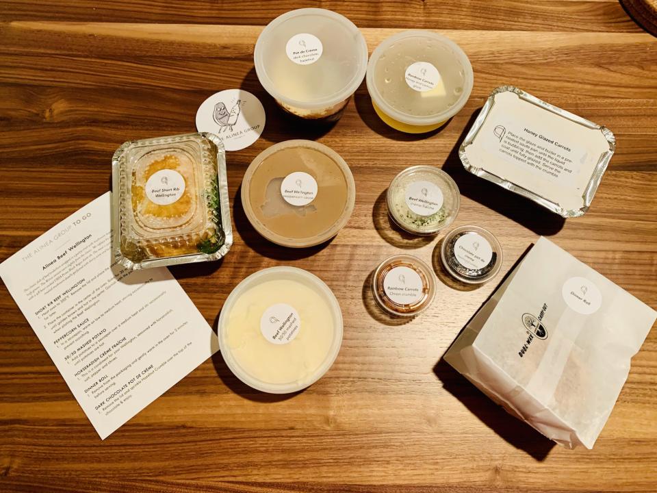 Unpacked meal in takeout boxes (plus instruction sheet) from Alinea laid out on wood table