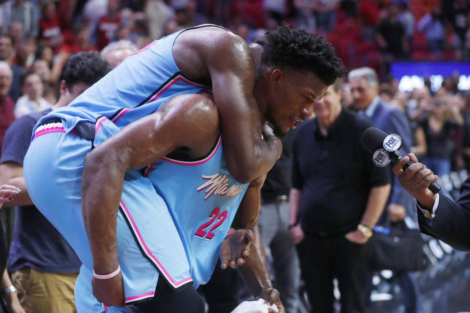 Miami Heat center Bam Adebayo jumps onto the back of forward Jimmy Butler as Butler is interviewed after the team's NBA basketball game against the Indiana Pacers, Friday, Dec. 27, 2019, in Miami. The Heat won 113-112. (AP Photo/Wilfredo Lee)