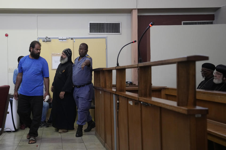 A police officer leads the two suspects appearing at the magistrate court in Cullinan, a town east of Pretoria, South Africa, Thursday, March 14, 2024. Two suspects appeared at the court for the murder of three Egyptian monks belonging to the Coptic Orthodox Church at a monastery in South Africa. (AP Photo/Themba Hadebe)