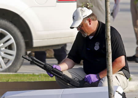 A police officer inspects a weapon removed from a vehicle in the parking lot of the Twin Peaks restaurant, where nine members of a motorcycle gang were shot and killed, in Waco, May 19, 2015. REUTERS/Mike Stone