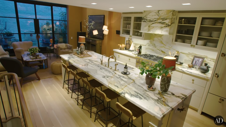 A kitchen with a long table with chairs around it  and comfy chairs at the other end of the room near full-length windows