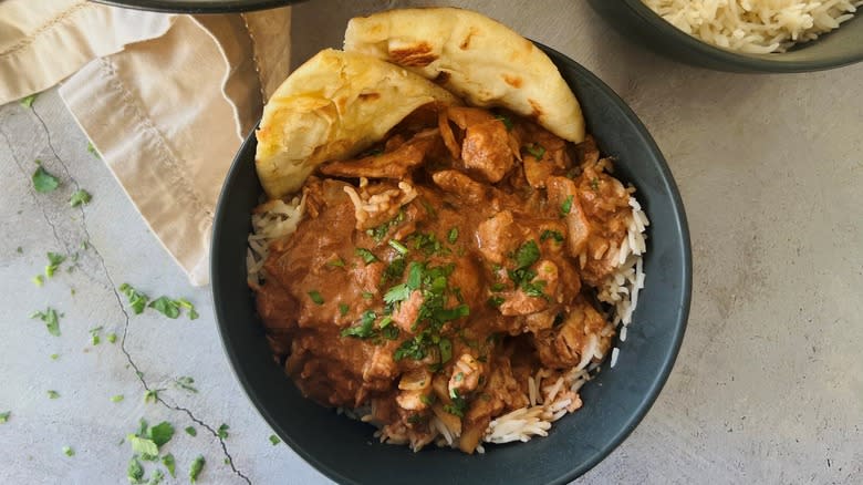 butter chicken in black bowl with pita bread