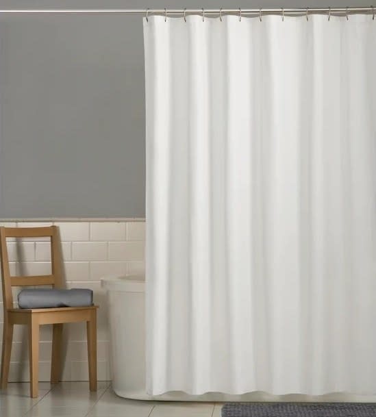 White shower curtain on a rod with a wooden chair in a bathroom setting