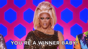 RuPaul in sparkling attire with text "You're a winner baby!" on a reality show set