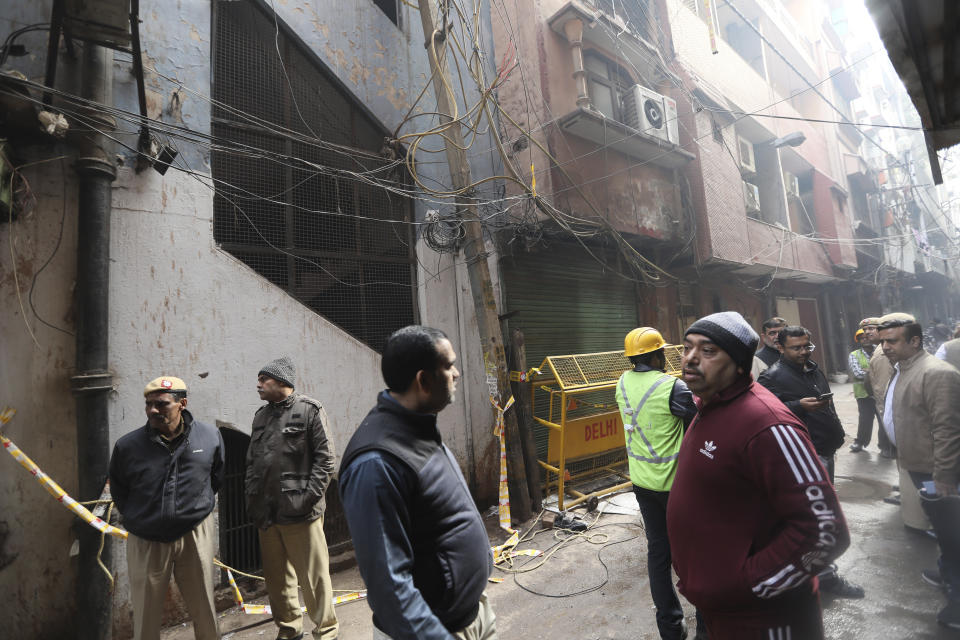 Policemen and neighbors stand in front of an ill-fated building which caught fire on Sunday, in New Delhi, India, Monday, Dec. 9, 2019. Authorities say an electrical short circuit appears to have caused a devastating fire that killed dozens of people in a crowded market area in central New Delhi. Firefighters fought the blaze from 100 yards away because it broke out in one of the area's many alleyways, tangled in electrical wire and too narrow for vehicles to access.(AP Photo/Manish Swarup)