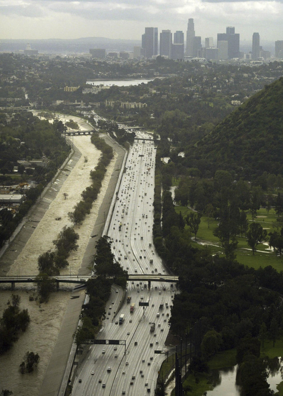 FILE - Surging water fills the Los Angeles River where it runs alongside the Golden State Freeway on Feb. 22, 2005. The river wanders through 14 cities from the San Fernando Valley through downtown Los Angeles and south to Long Beach, where it empties into the ocean. On Monday, Feb. 5, 2024, fed by a slow-moving atmospheric river dumping historic amounts of rain, the river was raging and even threatened to overspill its flood-control barriers in some sections. (AP Photo/Damian Dovarganes, File)