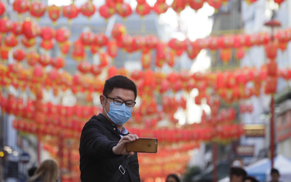 A man wears a mask as he takes a photograph in China Town in London, Friday, Feb. 7, 2020. The director-general of the World Health Organization says a drop in the number of new coronavirus cases for two days is “good news” but cautions against reading too much into that. China reported 31,161 cases in mainland China in its update Friday. (AP Photo/Kirsty Wigglesworth)