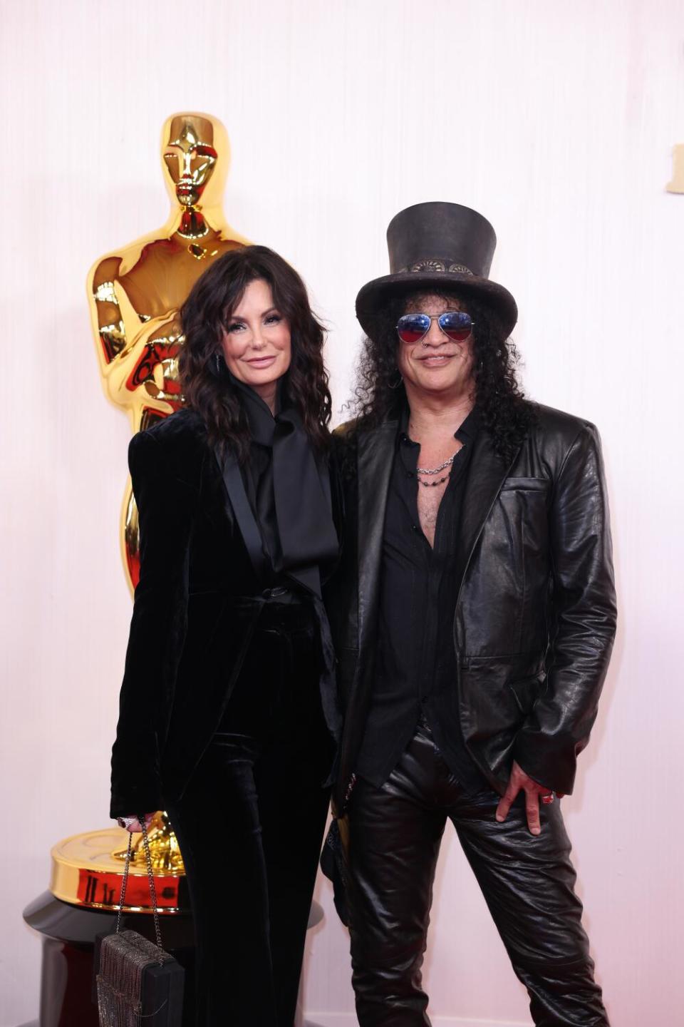 Meegan Hodges and Slash, both in black, pose in front of an Oscar statue.