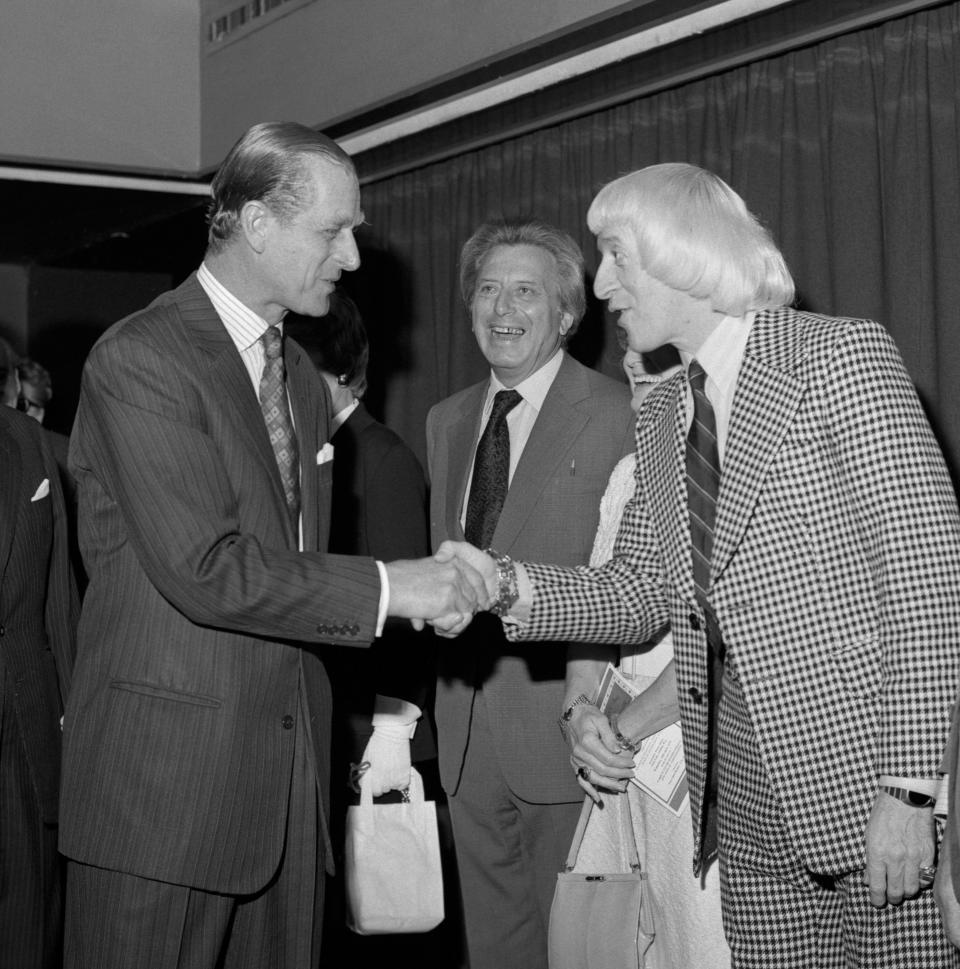 Guest of honour, The Duke of Edinburgh, shaking hands with show business personality Jimmy Savile (r), watched by Sir Bernard Delfont (c), at the Variety Club of Great Britain's luncheon. The luncheon was in aide of the Variety Club's National Sponsored Walk, part of the Club's International 1975 annual convention.   (Photo by PA Images via Getty Images)