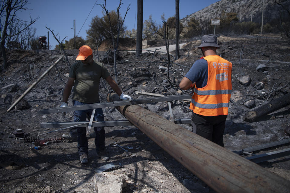 Workers of the electric company replace a utility pole after a wildfire in the Fyli suburb, northwest Athens, Greece, Friday, Aug. 25, 2023. Authorities battling a major wildfire in northeastern Greece that has been described as the European Union's largest single fire recorded have recovered another body, the fire department says, bringing the total death toll of wildfires in Greece this week to 21. (AP Photo/Michael Varaklas)