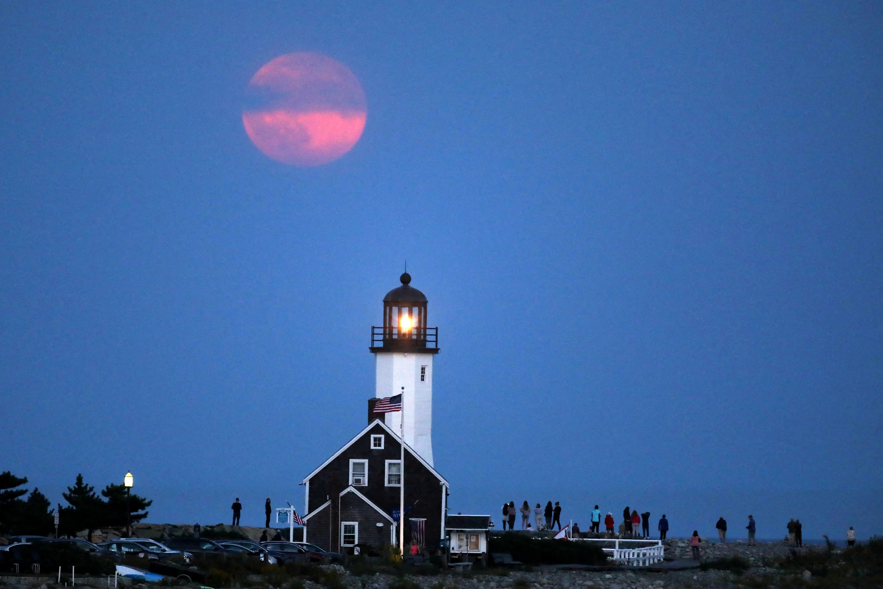 A harvest supermoon rises over a lighthouse in Scituate, Mass., on Tuesday.