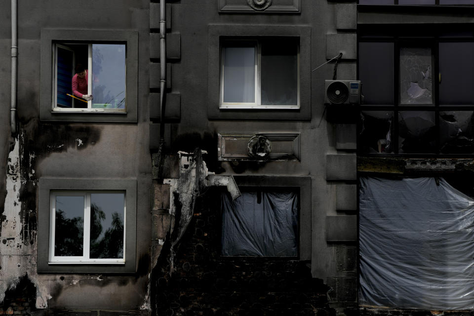 A woman cleans a window of her home ruined by shelling, in Bucha, on the outskirts Kyiv, Ukraine, Wednesday, May 25, 2022. (AP Photo/Natacha Pisarenko)