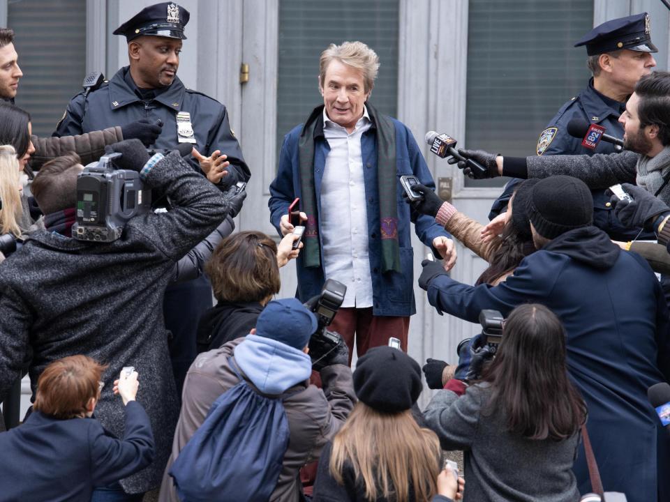 Oliver stands on the courthouse steps surrounded by police and reporters in this still from season 2 of Hulu's "Only Murders in the Building."