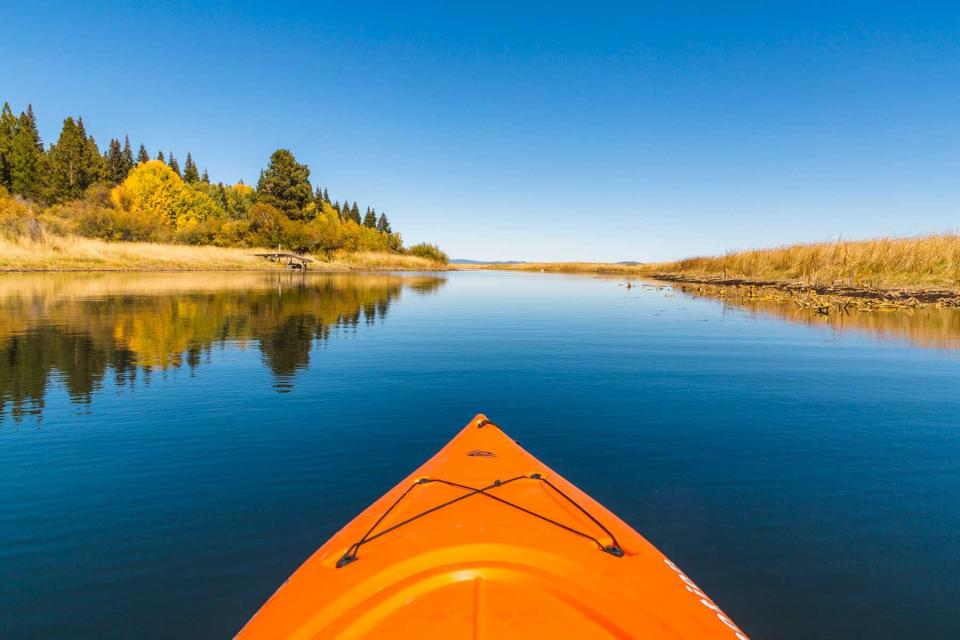 Orange kayak enjoying the smooth blue water of Lower Klamath Lake and fall foliage.