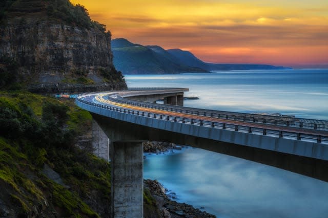 Sunset over the Sea cliff bridge along Australian Pacific ocean coast with lights of passing cars