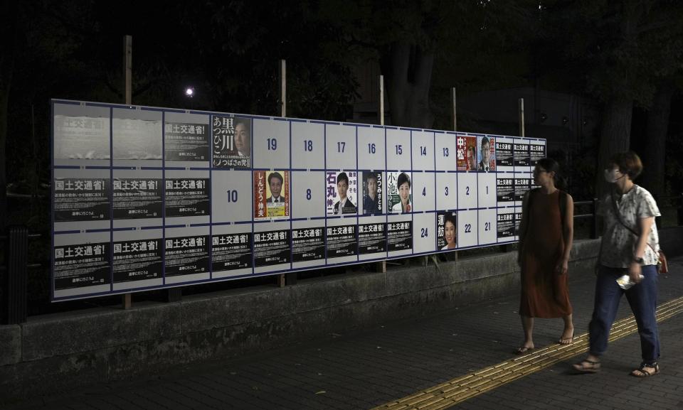 People walk by an election poster board for Tokyo gubernatorial election in Tokyo, on June 20, 2024. Tokyo elects a new governor on Sunday, July 7, but residents say personal publicity stunts have overtaken serious campaigning to a degree never seen before. There are nearly nude women in suggestive poses, pets, an AI character and a man practicing his golf swing. (Kyodo News via AP)