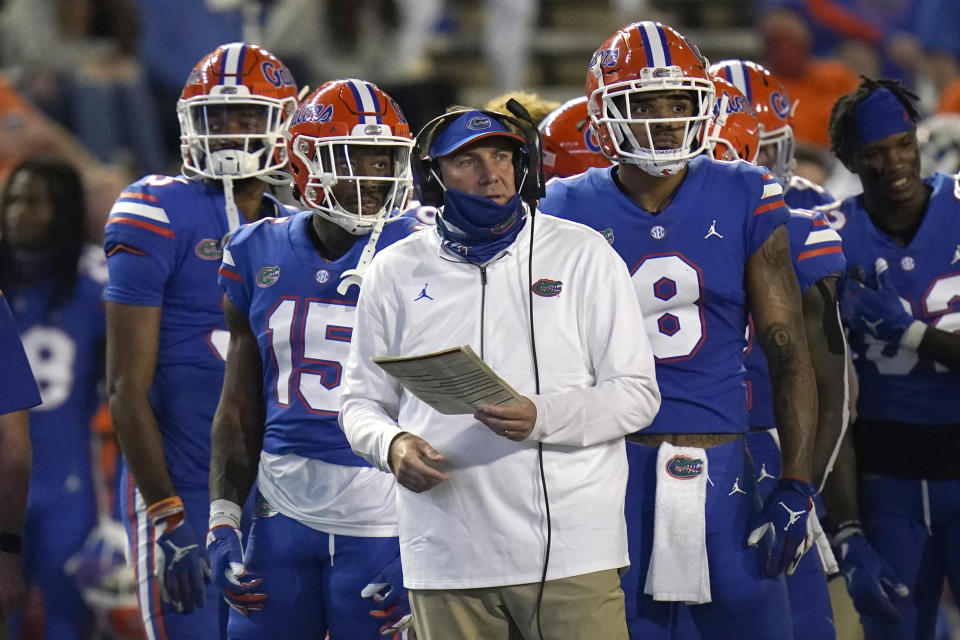 Florida head coach Dan Mullen stands on the sideline in front of a few Florida football players.