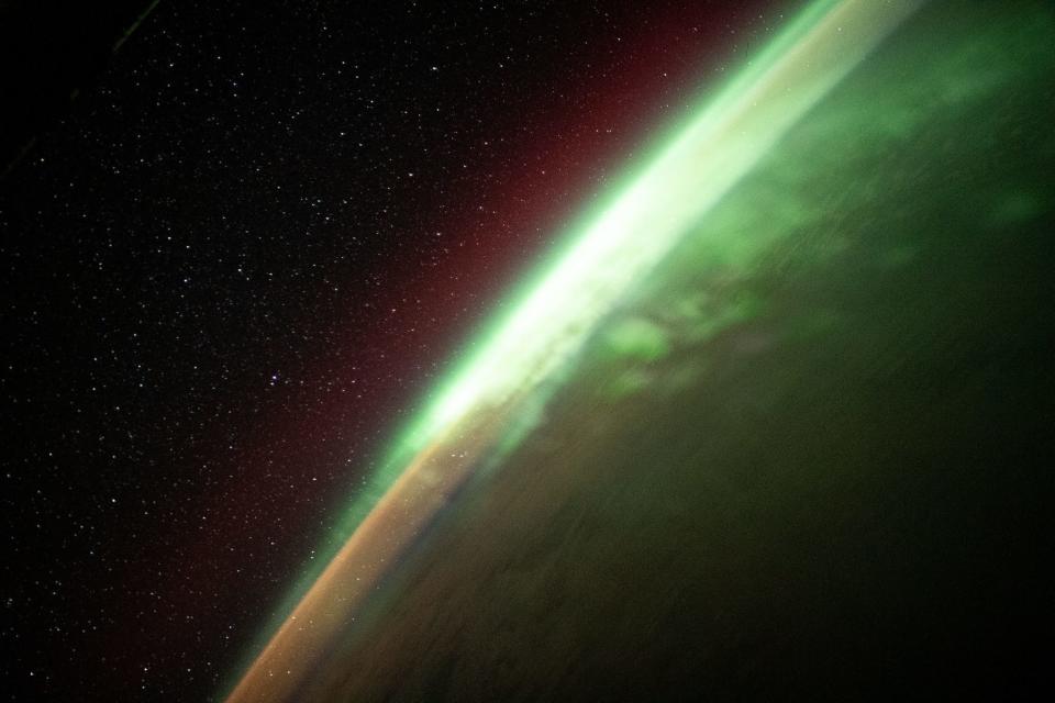 aurora green glow lines the curvature of the earth with starry outer space behind it