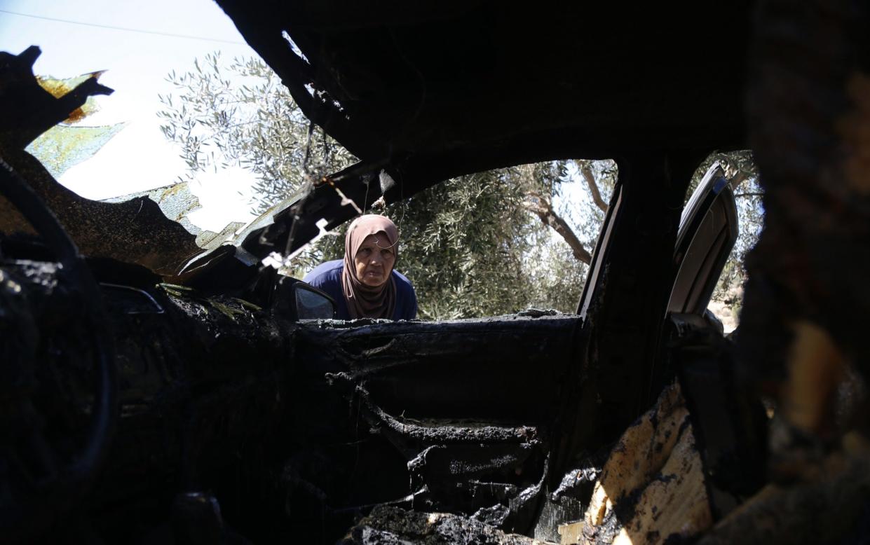 Palestinians look at the vehicle which was burnt down after an Israeli raid in the West Bank