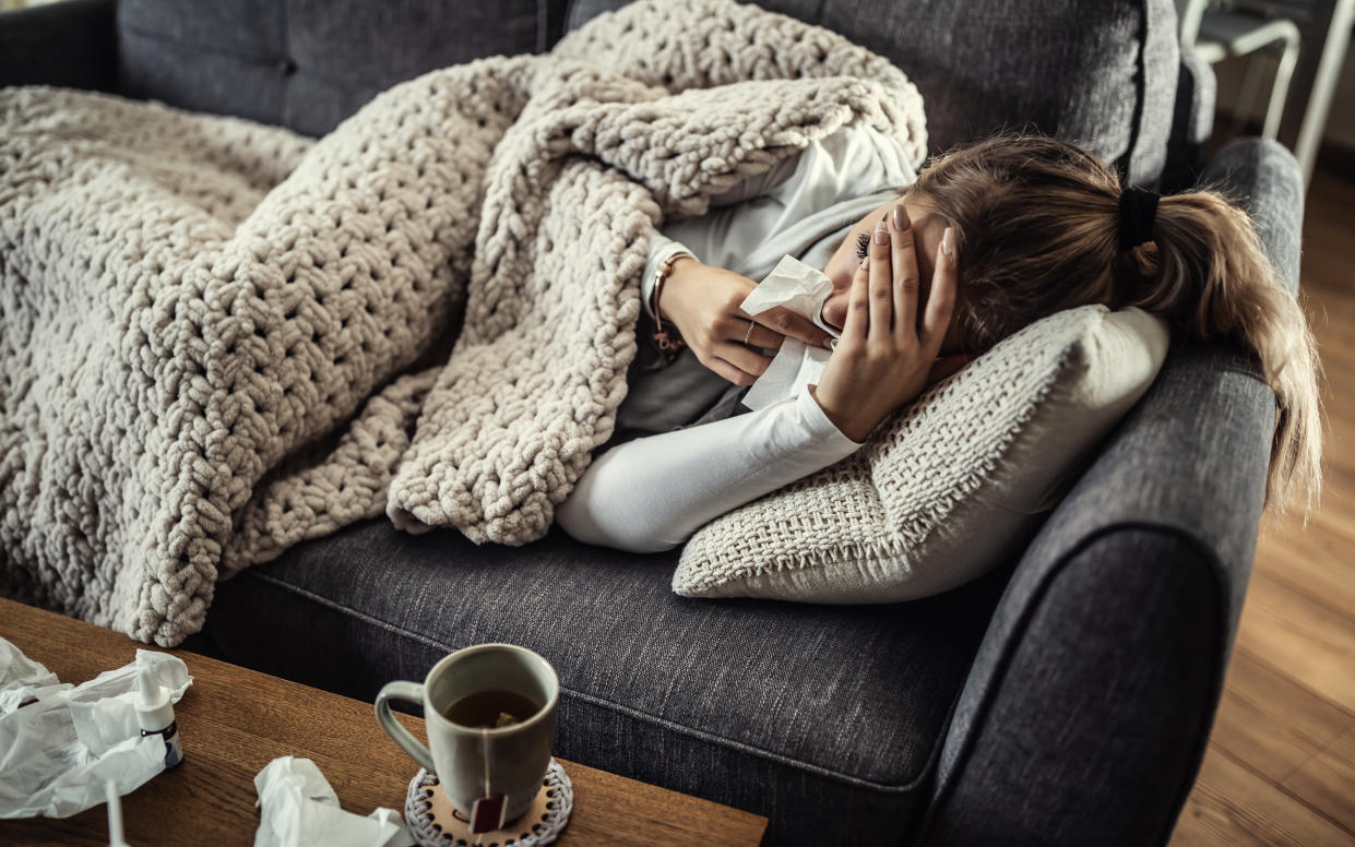 woman laying on sofa looking sick with flu/Norovirus with blanket