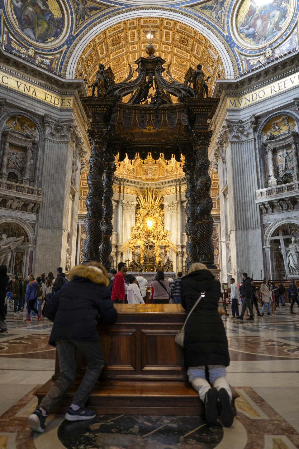 People pray in front of the 17th century, 95ft-tall bronze canopy by Giovan Lorenzo Bernini surmounting the papal Altar of the Confession in St. Peter's Basilica at the Vatican, Wednesday, Jan. 10, 2024. Vatican officials unveiled plans Thursday, Jan.11, for a year-long, 700,000 euro restoration of the monumental baldacchino, or canopy, of St. Peter's Basilica, pledging to complete the first comprehensive work on Bernini's masterpiece in 250 years before Pope Francis' big 2025 Jubilee. (AP Photo/Andrew Medichini)