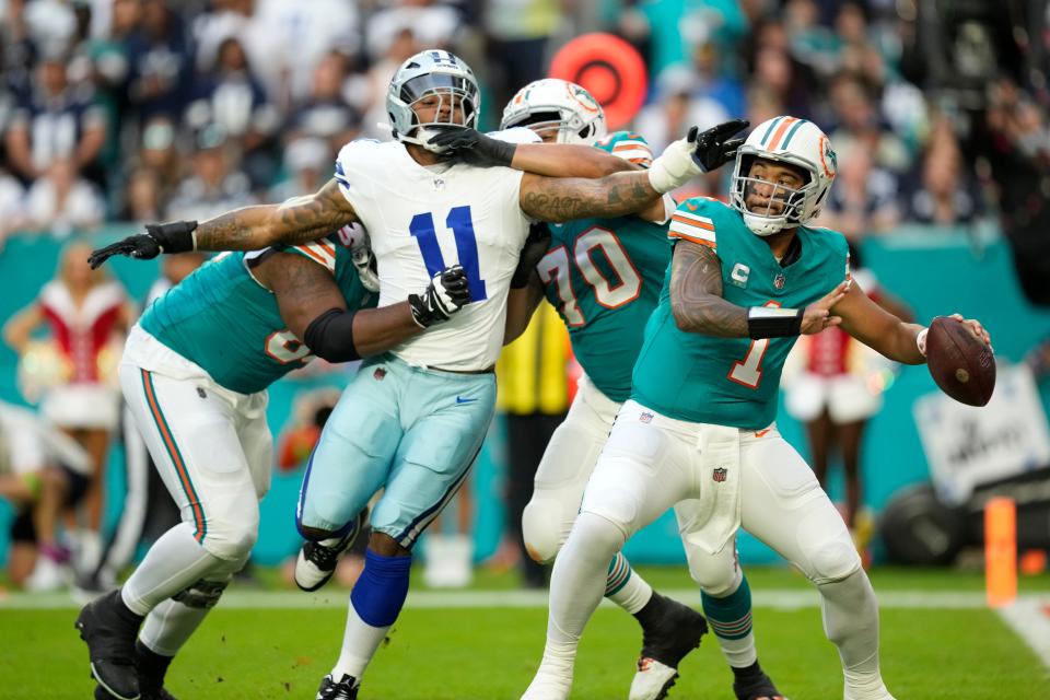 Miami Dolphins quarterback Tua Tagovailoa (1) stands back to pass as Dallas Cowboys linebacker Micah Parsons (11) is held back by offensive tackle Kendall Lamm (70) during the first half of an NFL football game, Sunday, Dec. 24, 2023, in Miami Gardens, Fla.