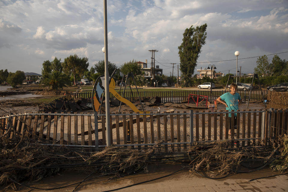 A boy stands behind a fence of a destroyed playground following a storm at the village of Bourtzi, on Evia island, northeast of Athens, on Sunday, Aug. 9, 2020. Five people, including en elderly couple and an 8-month-old baby have been found dead, two more are missing and dozens have been trapped in their homes and cars as a storm hits the island of Evia in central Greece, authorities said Sunday. (AP Photo/Yorgos Karahalis)