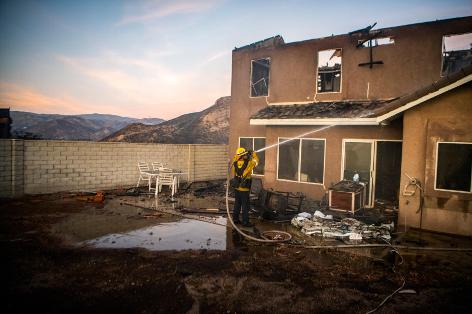 A firefighter hoses down a damaged house as the Tick Fire burns in the Santa Clarita, Calif., area on Oct. 24, 2019. | Stuart W. Palley