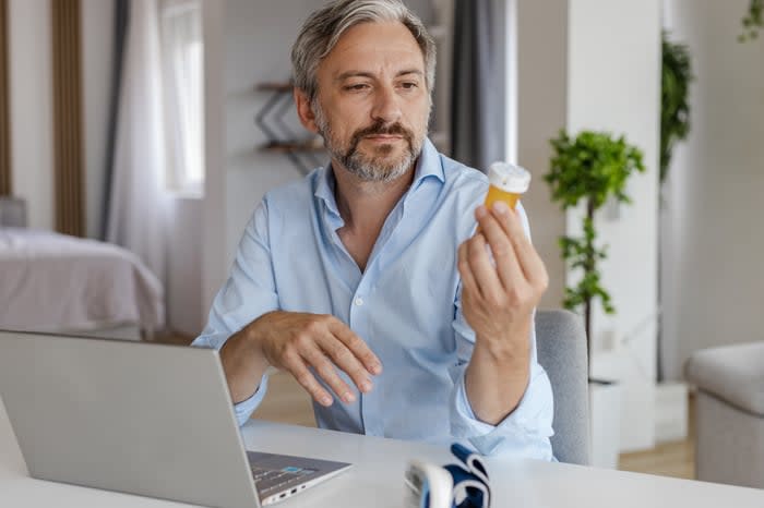 Person holding pill bottle in front of laptop.