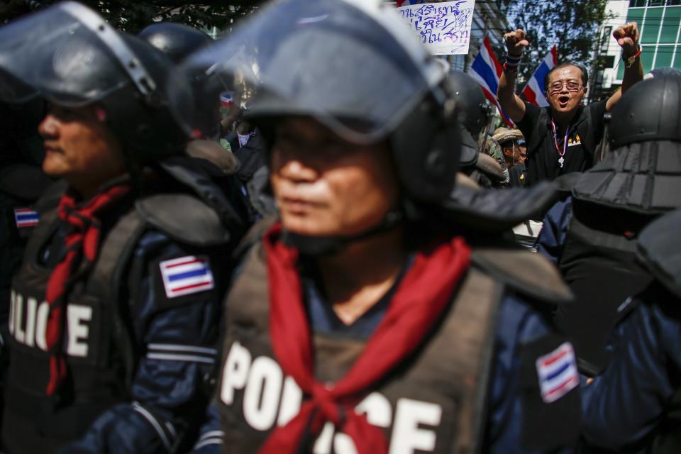 An anti-government protester shouts slogans as riot policemen stand guard outside the headquarters of the ruling Puea Thai Party of Prime Minister Yingluck Shinawatra in Bangkok