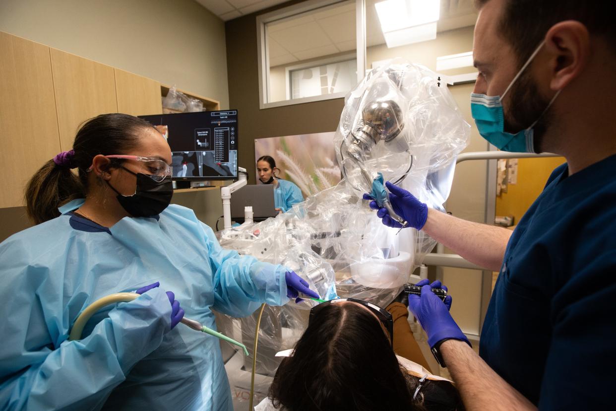 Adam Marina, right, dentist at Aspen Dental, 1730 S.W. Wanamaker Road, guides the robotic arm from a YOMI machine to Karly Baird's mouth Monday as dental assistants Shantel Kingcannon, left, and Courtney Fulton help with the demonstration. Marina was showing how the robot works to safely drill and assist in dental implants.