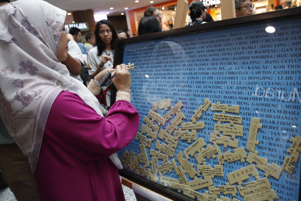 A woman writes a message near the jigsaw puzzle board during the tenth annual remembrance event at a shopping mall, in Subang Jaya, on the outskirts of Kuala Lumpur, Malaysia, Sunday, March 3, 2024. Ten years ago, a Malaysia Airlines Flight 370, had disappeared March 8, 2014 while en route from Kuala Lumpur to Beijing with 239 people on board. (AP Photo/FL Wong)