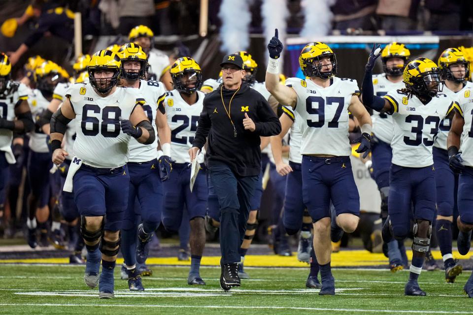 Michigan head coach Jim Harbaugh runs onto the field with his team before the Big Ten championship against Iowa.