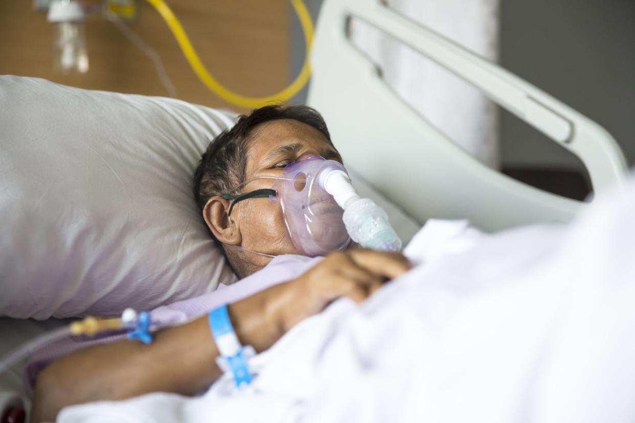 Old woman patient lying on Hospital bed with ventilator mask on her nose. She has her eyes closed.